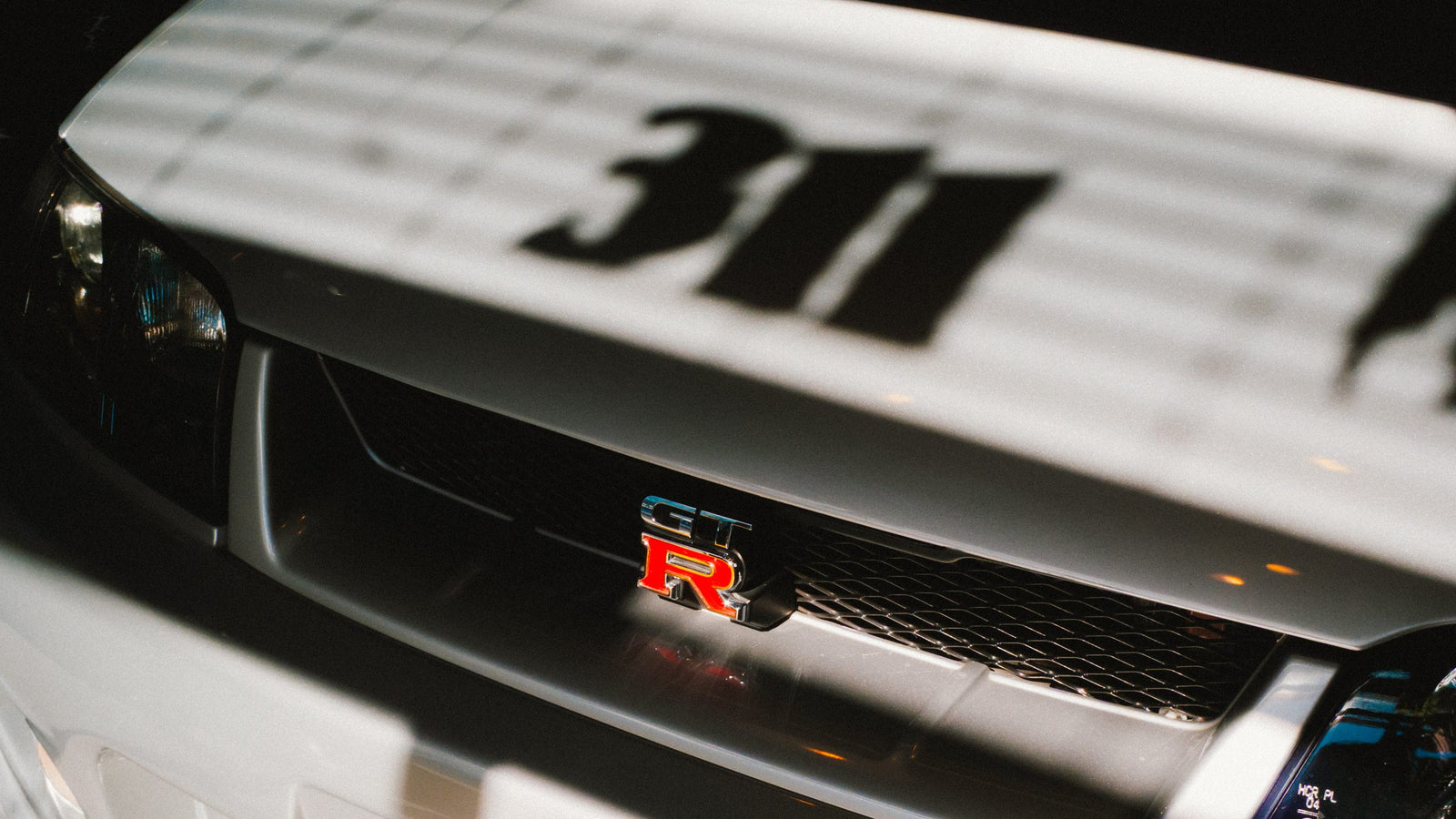 The grille of a white Nissan GT-R with the 311 window lettering shadowed across the hood